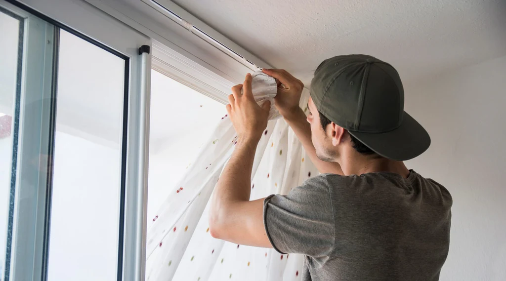 man-in-cap-installing-white-sheer-curtains-onto-ceiling-mounted-track